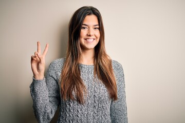 Poster - Young beautiful girl wearing casual sweater standing over isolated white background smiling with happy face winking at the camera doing victory sign. Number two.