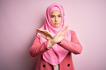 Poster - Young beautiful girl wearing muslim hijab standing over isolated pink background Rejection expression crossing arms and palms doing negative sign, angry face