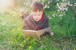 © Olga - A teenage European boy is lying on the grass and reading an interesting book on a spring or summer day.