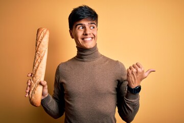 Poster - Young handsome man holding homemade fresh bread over isolated yellow background pointing and showing with thumb up to the side with happy face smiling