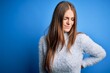 © Krakenimages.com - Young beautiful redhead woman wearing casual sweater over isolated blue background Suffering of backache, touching back with hand, muscular pain