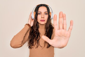 Wall Mural - Young beautiful woman with blue eyes listening to music and dancing using headphones with open hand doing stop sign with serious and confident expression, defense gesture