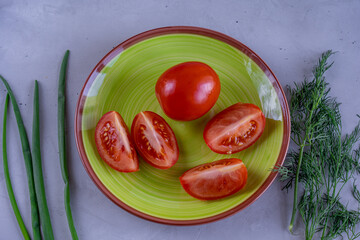Wall Mural - Sliced tomatoes on green plate surrounded by fresh green onion and dill