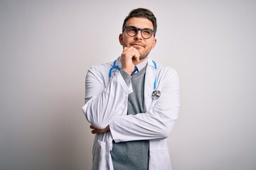 Wall Mural - Young doctor man with blue eyes wearing medical coat and stethoscope over isolated background with hand on chin thinking about question, pensive expression. Smiling and thoughtful face. Doubt concept.