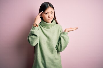 Sticker - Young beautiful asian woman wearing green winter sweater over pink solated background confused and annoyed with open palm showing copy space and pointing finger to forehead. Think about it.