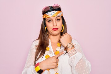 Wall Mural - Young hispanic hippie woman wearing fashion boho style and sunglasses over pink background In hurry pointing to watch time, impatience, looking at the camera with relaxed expression