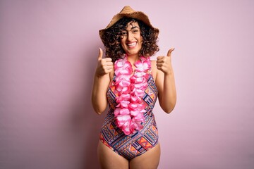 Sticker - Young beautiful arab woman on vacation wearing swimsuit and hawaiian lei flowers success sign doing positive gesture with hand, thumbs up smiling and happy. Cheerful expression and winner gesture.