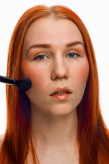 close beauty portrait of a red-haired girl with a brush for applying makeup. Isolated on a white background.