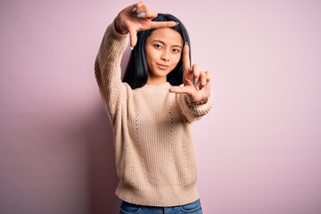 Young beautiful chinese woman wearing casual sweater over isolated pink background smiling making frame with hands and fingers with happy face. Creativity and photography concept.