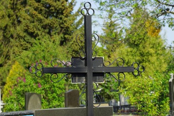 one black iron cross in a cemetery among green trees