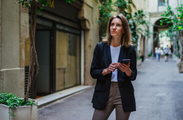 Wall Mural - business woman booking hotel during business trip using internet technologies her mobile phone, female tourist holding in hands smartphone planning trip in old town europe city