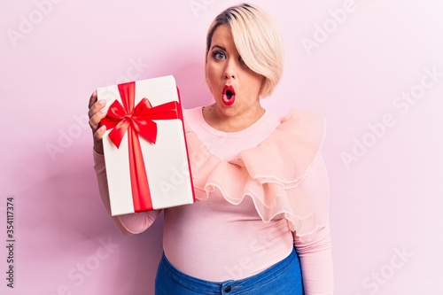 Fotografía Young beautiful blonde plus size woman holding birthday gift over isolated pink