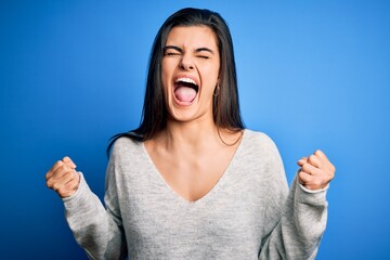 Wall Mural - Young beautiful brunette woman wearing casual sweater standing over blue background excited for success with arms raised and eyes closed celebrating victory smiling. Winner concept.