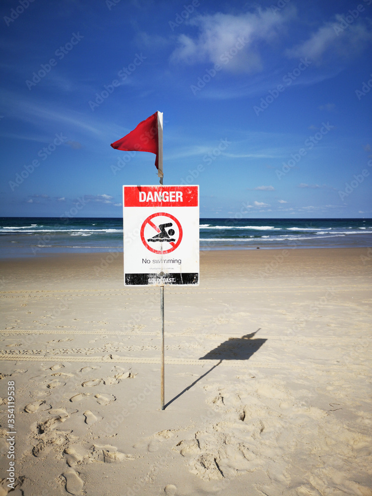 Danger No Swimming information sign with a red flag near the ocean in ...