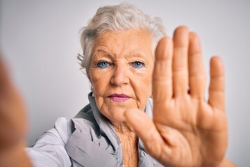 Wall Mural - Senior beautiful grey-haired woman making selfie by camera over isolated white background with open hand doing stop sign with serious and confident expression, defense gesture