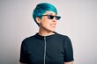 © Krakenimages.com - Young woman with blue fashion hair wearing thug life sunglasses over white background looking away to side with smile on face, natural expression. Laughing confident.
