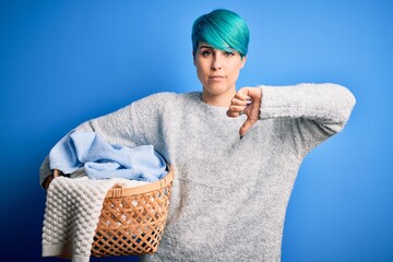 Sticker - Young woman with blue fashion hair doing domestic chores holding wicker laundry basket with angry face, negative sign showing dislike with thumbs down, rejection concept