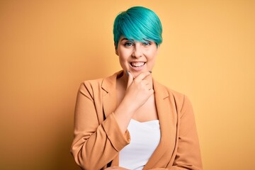 Sticker - Young beautiful woman with blue fashion hair wearing casual jacket over yellow background looking confident at the camera smiling with crossed arms and hand raised on chin. Thinking positive.