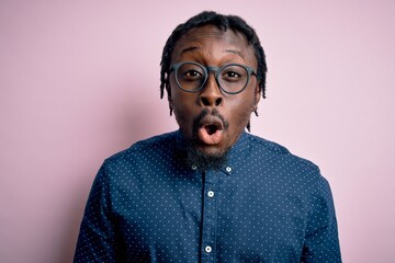 Sticker - Young handsome african american man wearing casual shirt and glasses over pink background afraid and shocked with surprise expression, fear and excited face.