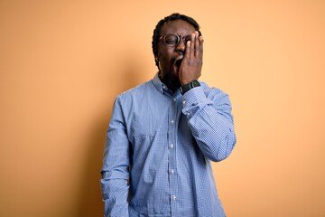 Poster - Young handsome african american man wearing shirt and glasses over yellow background Yawning tired covering half face, eye and mouth with hand. Face hurts in pain.