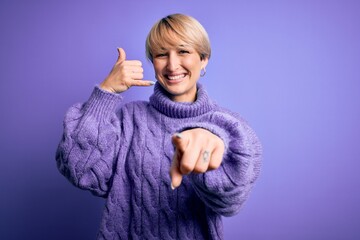 Poster - Young blonde woman with short hair wearing winter turtleneck sweater over purple background smiling doing talking on the telephone gesture and pointing to you. Call me.