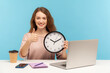 Good job, time to work! Positive happy woman, satisfied office employee sitting at workplace, holding big clock and showing thumbs up, like gesture. indoor studio shot isolated on blue background