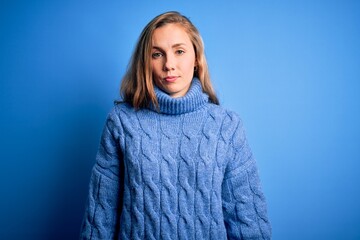 Poster - Young beautiful blonde woman wearing casual turtleneck sweater over blue background Relaxed with serious expression on face. Simple and natural looking at the camera.