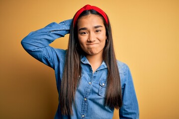 Poster - Young beautiful asian woman wearing casual denim shirt and diadem over yellow background confuse and wonder about question. Uncertain with doubt, thinking with hand on head. Pensive concept.