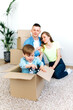 Relocation. Moving to a new home. Happy family have fun in their new home, parents plays with their baby which sitting in a cardboard box and playing with a toy car