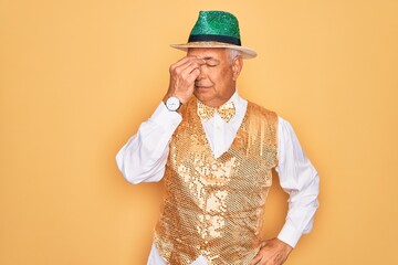 Wall Mural - Middle age senior grey-haired man wearing Brazilian carnival custome over yellow background tired rubbing nose and eyes feeling fatigue and headache. Stress and frustration concept.