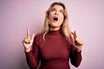 Sticker - Young beautiful blonde woman wearing casual sweater over isolated pink background amazed and surprised looking up and pointing with fingers and raised arms.