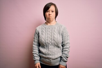 Wall Mural - Young down syndrome woman wearing casual sweater over isolated background puffing cheeks with funny face. Mouth inflated with air, crazy expression.