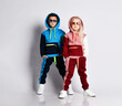 Little kids, boy and girl, in sunglasses and hoods, colorful tracksuits, sneakers. They posing isolated on white studio background