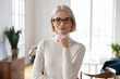 Head shot attractive young smiling blonde businesswoman in glasses touching chin, looking at camera. Portrait of successful 30s businessowner leader professional specialist, standing on modern office.