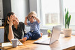 © Vadim Pastuh - Freelancer mom trying to work at home with a laptop, a toddler boy is snatching her eyeglasses and playing. It's hard to concentrate on work with a child