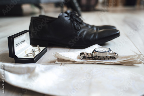 Fototapeta na szkło Side view of groom's accessories. black leather shoes, luxury metal watches laying on white handkerchief, anchor shape cufflinks in padded box.