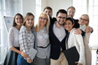 © fizkes - Portrait of emotional positive bonding diverse business people, posing for photo in office. Overjoyed excited friendly young and middle aged mixed race teammates embracing, looking at camera.