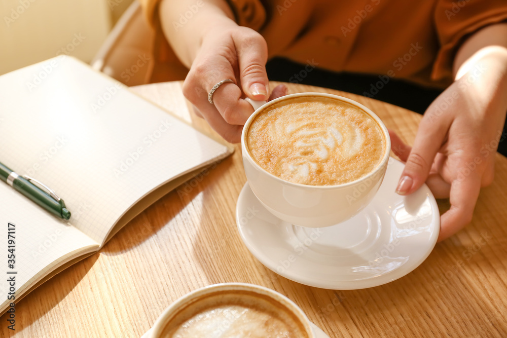Woman drinking tasty coffee at table in cafe