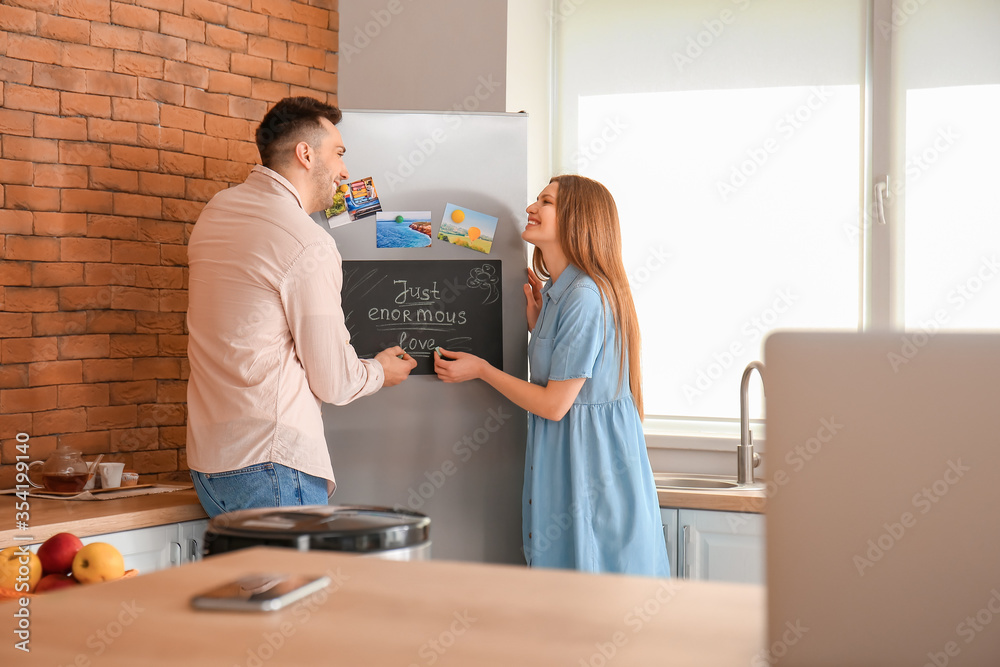 Happy couple near chalkboard on refrigerator in kitchen