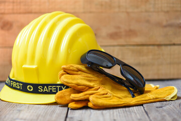 Safety equipment standard construction safety - Industrial protective workwear tool with yellow hat safety helmet glasses and gloves on wood background