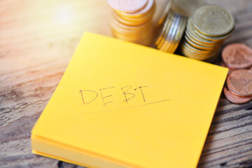 Debt concept with write debt on paper and stacked coins on wooden table background /