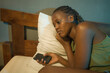 © TheVisualsYouNeed - dramatic lifestyle portrait of young sad and depressed black afro American woman crying in bed holding mobile phone victim of cyber bullying or broken heart in her bedroom