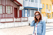 © Elena Sistaliuk - Beautiful young female smiling while standing near typical colorful buildings on street of Costa Nova, Aveiro, Portugal