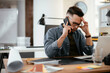 © JustLife - Businessman in office. Handsome man talking on phone at work.