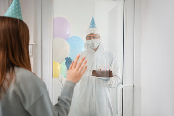 Canvas Print - Asian man in biohazard suit and with Birthday cake visiting his friend. Concept of epidemic