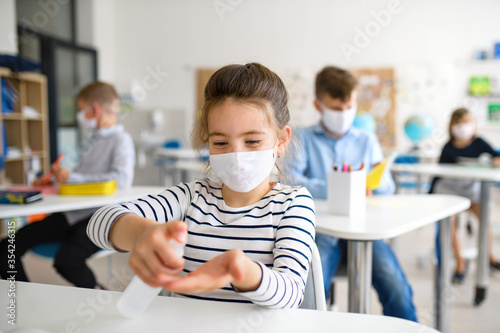 Fotomural Small girl with face mask at school after covid-19 lockdown, disinfecting hands