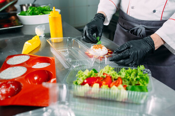 Food delivery in the restaurant. The chef prepares food in the restaurant and packs it in disposable dishes.