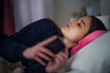 Wall Mural - Sad young girl with smartphone lying indoors on bed, online dating concept.