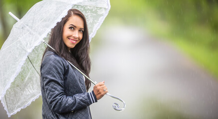 Wall Mural - Beautiful female smiles at the camera with an umbrella on her shoulder outdoors