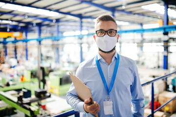 Technician or engineer with protective mask working in industrial factory, standing.